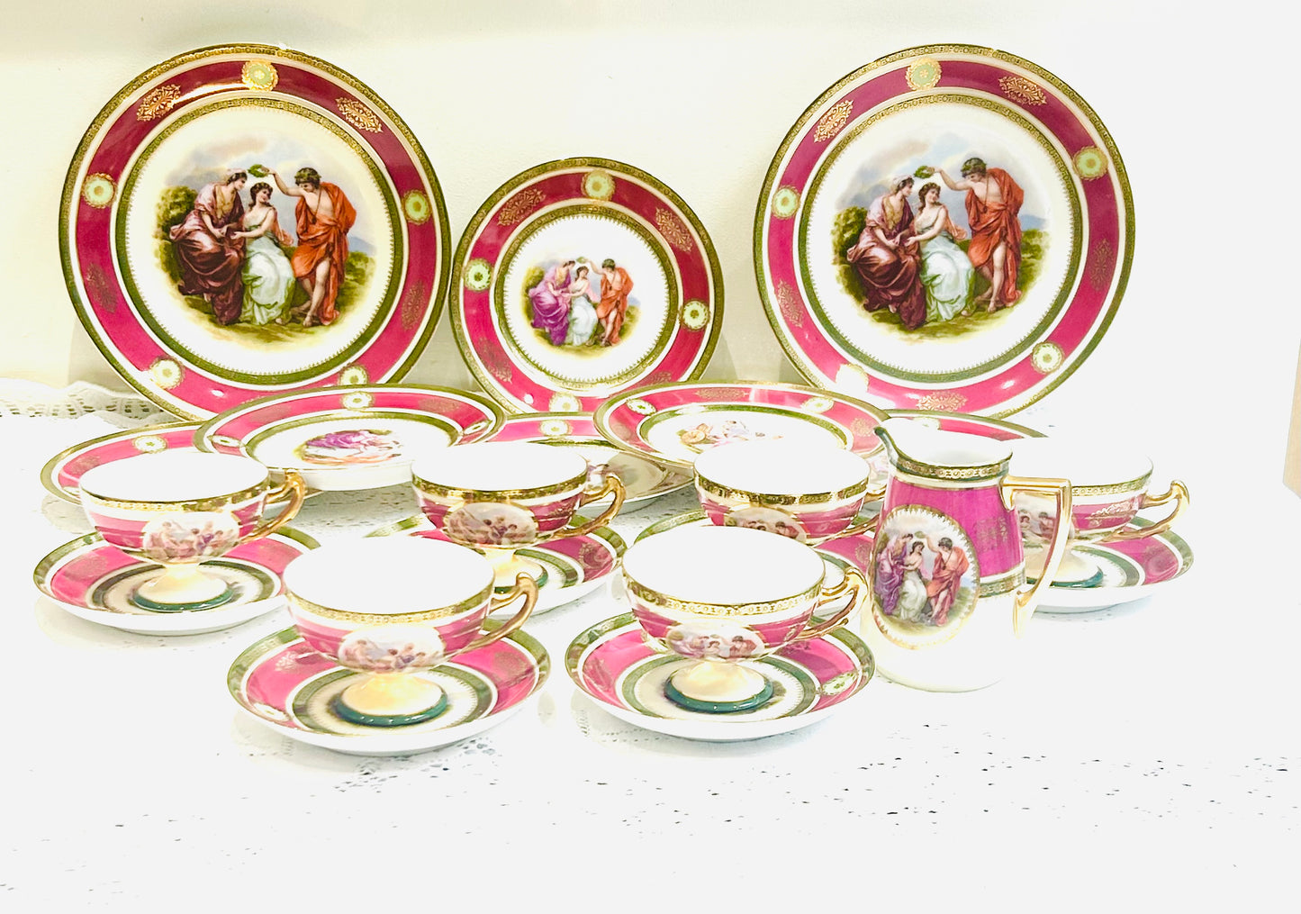 Vintage EPIAG porcelain tea set with magenta and gold borders, romantic figural scenes, and gilded accents on a lace-covered table